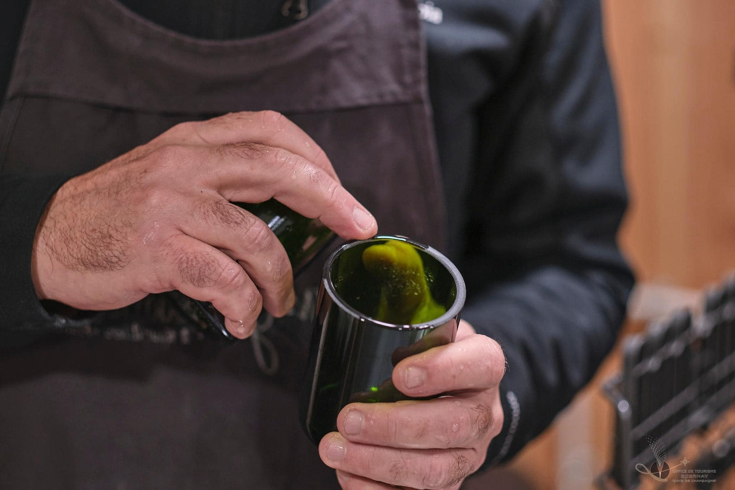 Deux mains d'un homme qui tiennent un flacon de bouteille de champagne coupé en deux. Il vérifie la qualité du ponçage de la future bougie.