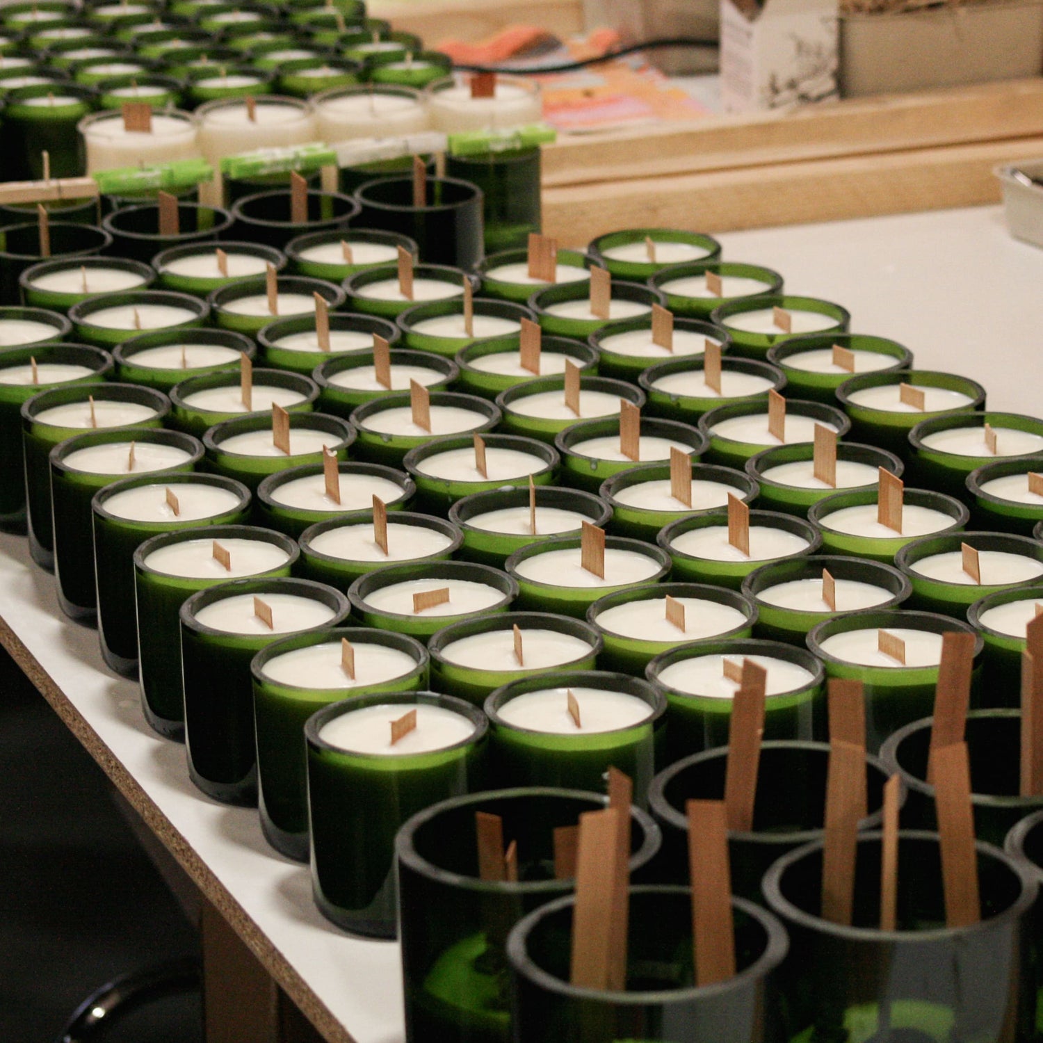 Nombreuses bougies Marsault coulées dans des fonds de bouteilles de champagnes, présentées sur une table de production avant de passer à l'étape de nettoyage