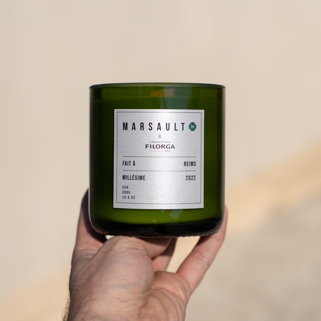 Main qui tient un exemplaire de bougie de la collaboration entre Marsault et Filorga qui est une célèbre entreprise de cosmétique.
